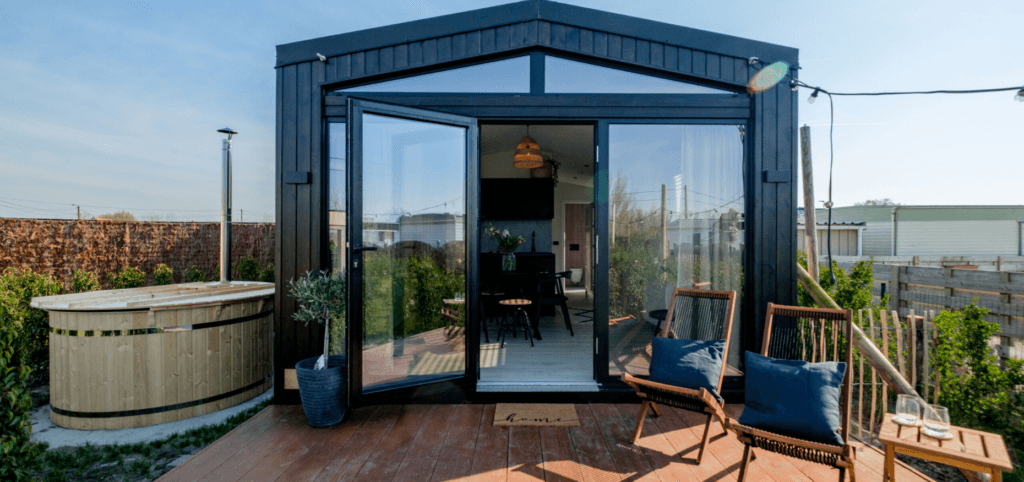 Moderne mantelzorgwoning met houten terras, openslaande glazen deuren, comfortabele stoelen en een natuurlijke tuinomgeving – een sfeervol en zelfstandig thuis op eigen erf